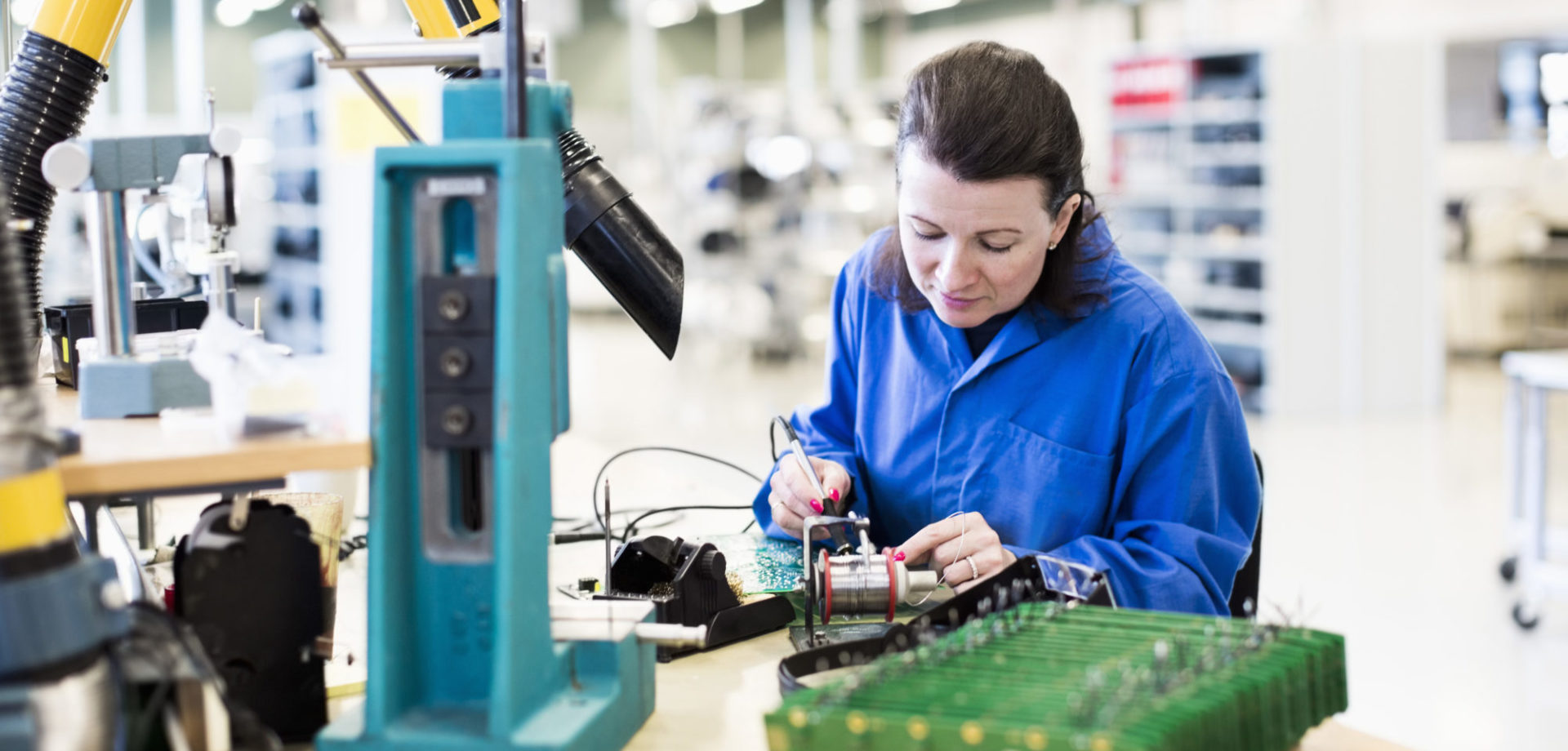 Mid adult female electrician working on circuit board at desk in industry