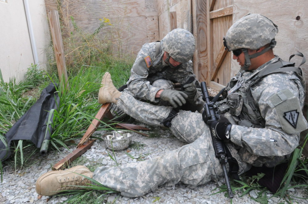 Bildet viser en soldat som plasserer årepressen på foten til en annen soldat.