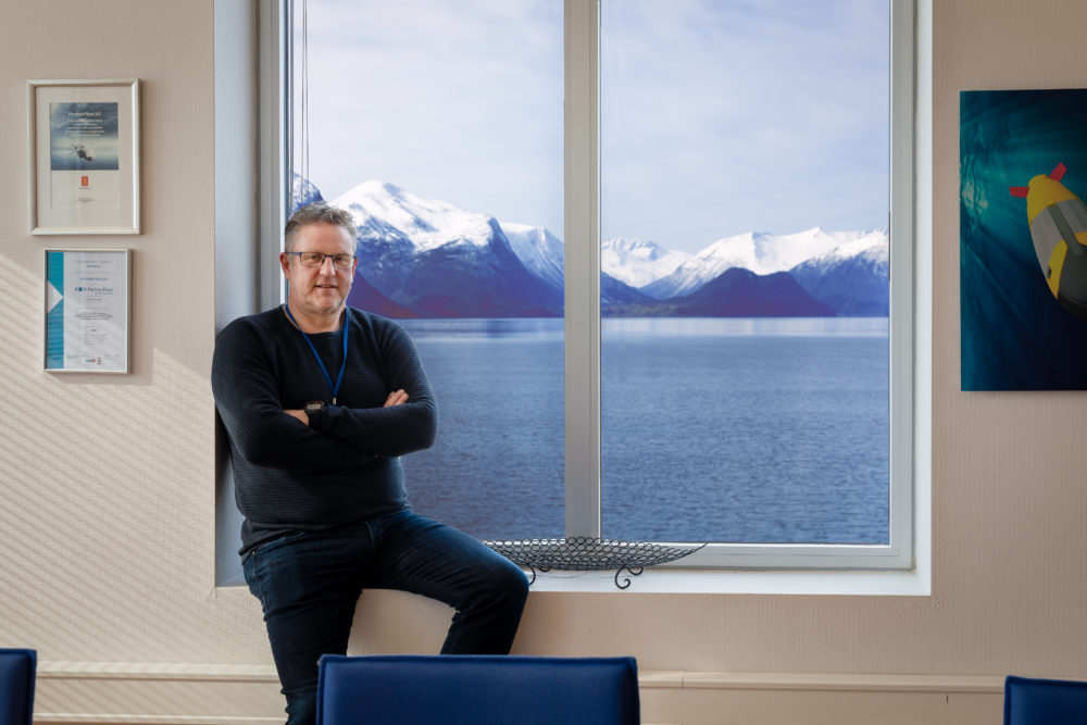 Bildet viser Tom Samuelsen sittende i en vinduskrok foran utsikten over Romsdalsfjorden