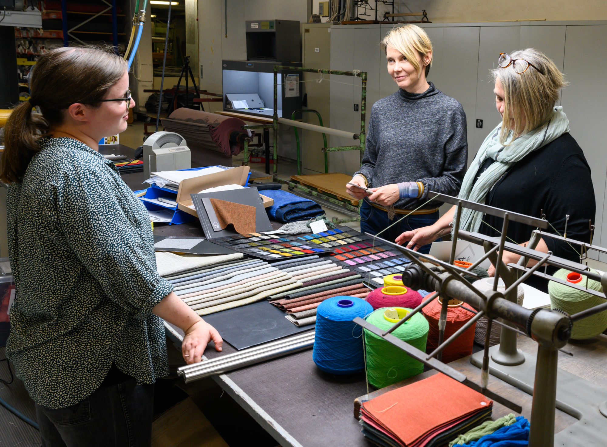Bildet viser tre damer som står og ser på fargeprøver i fabrikken til Innvik
