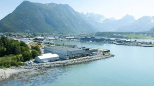 Oversiktsbilde av et industribygg som ligger i vakker natur med fjord og fjell.