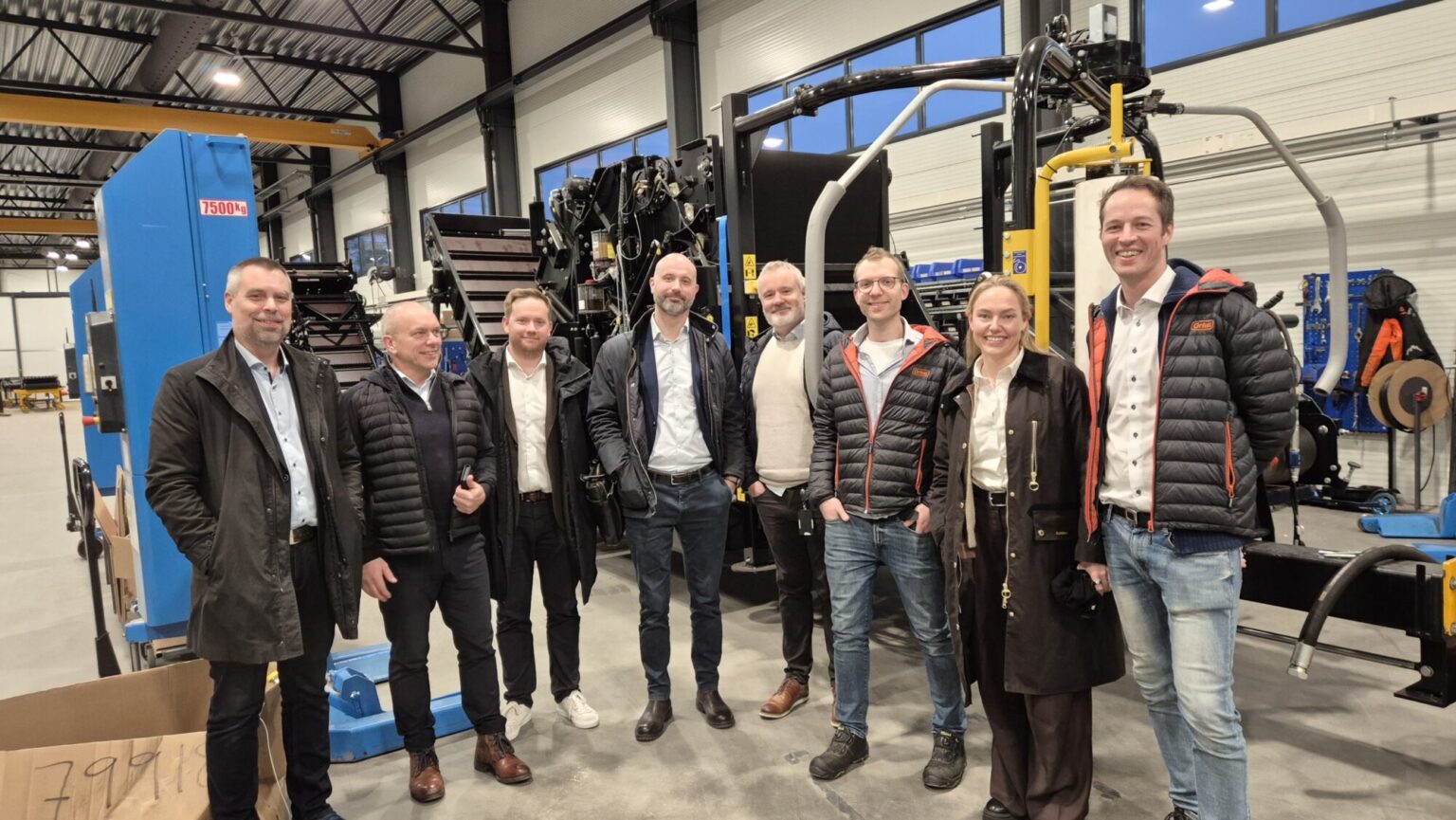 Bildet viser en gruppe bestående av seks menn og en dame som står i en verkstedshall